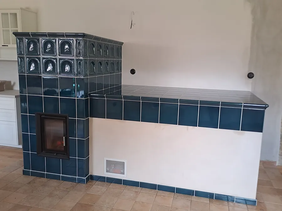 Kachlová kamna s tmavě modrými kachli, prosklenými dvířky a navazující sedací lavicí